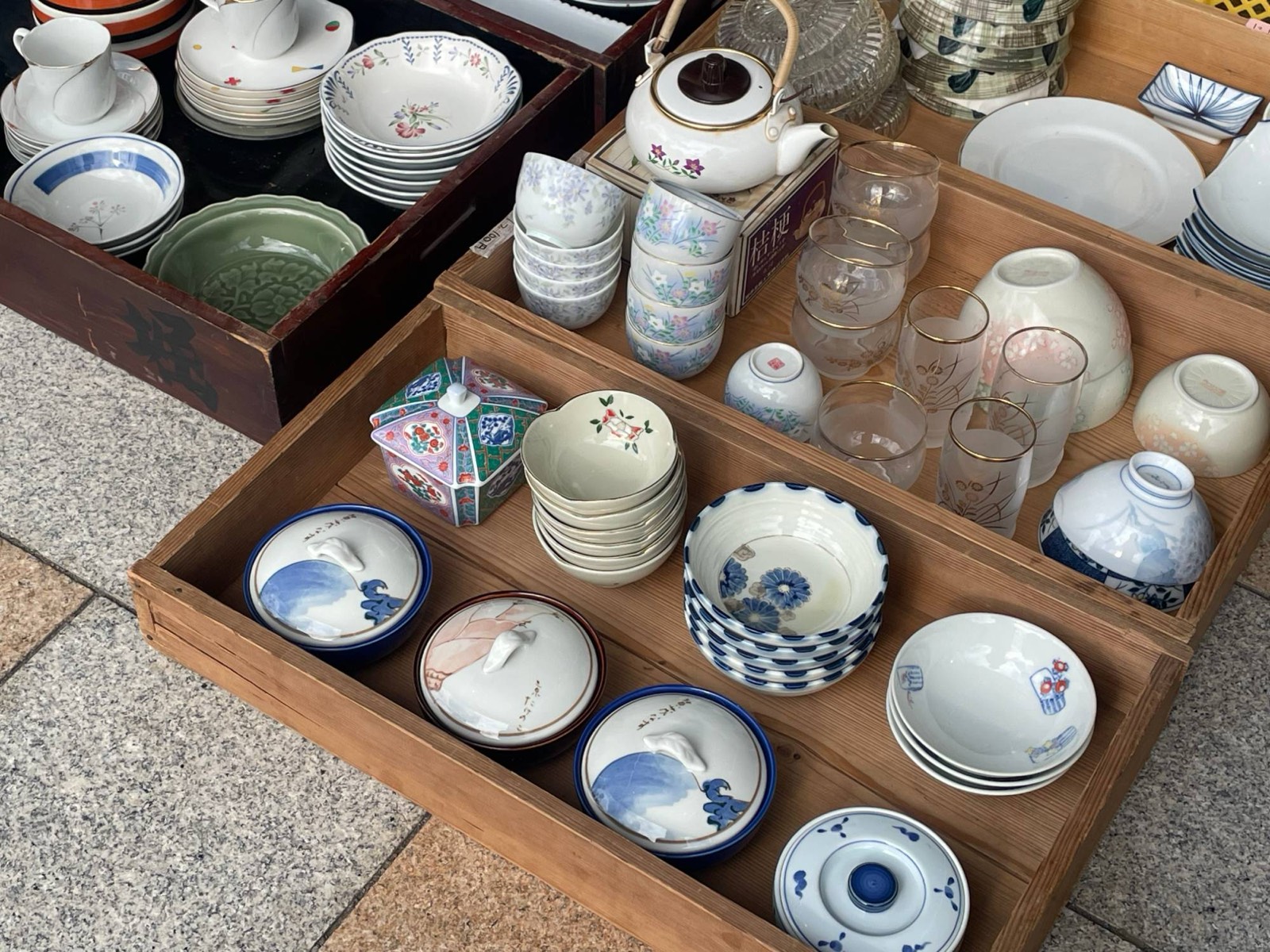木箱に並べた、さまざまな絵柄の食器や湯のみ、ガラスのコップ